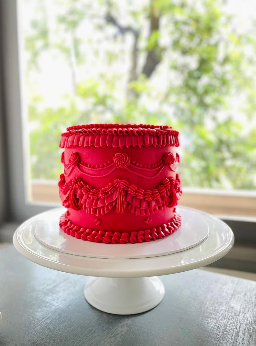 A tall red Lambeth cake piped with buttercream ruffles and swags
